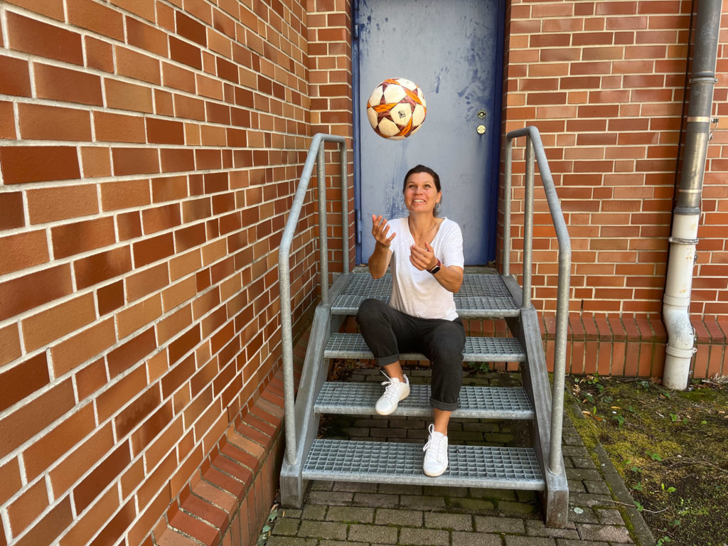 Louise Hansen sitzend auf einer Eisentreppe und dabei einen Ball hochwerfend.