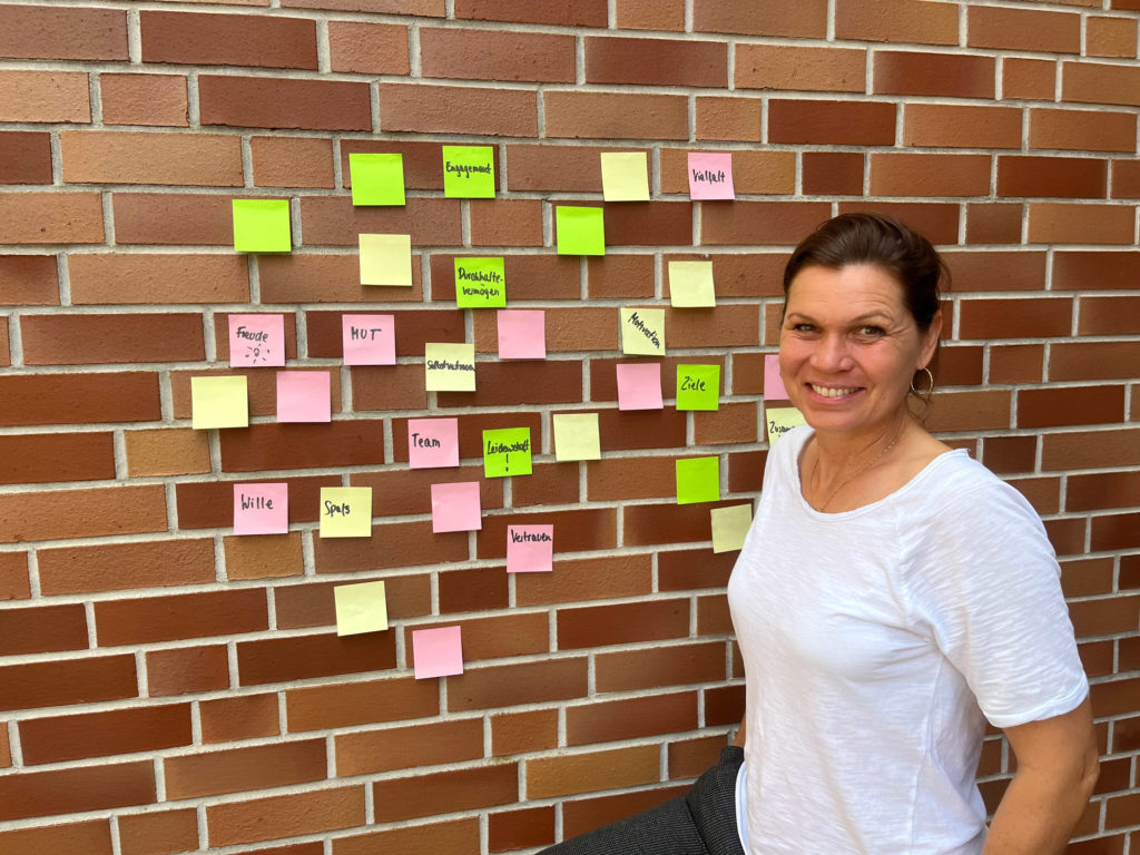 Louise Hansen stehend vor einer Hauswand, an der verschiedenfarbige Post-its kleben